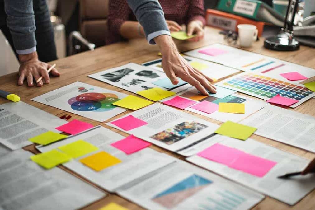 Brand-Husl-Image showcasing a collaborative workspace with people discussing branding concepts, colour palettes, and visual elements on a wooden table.