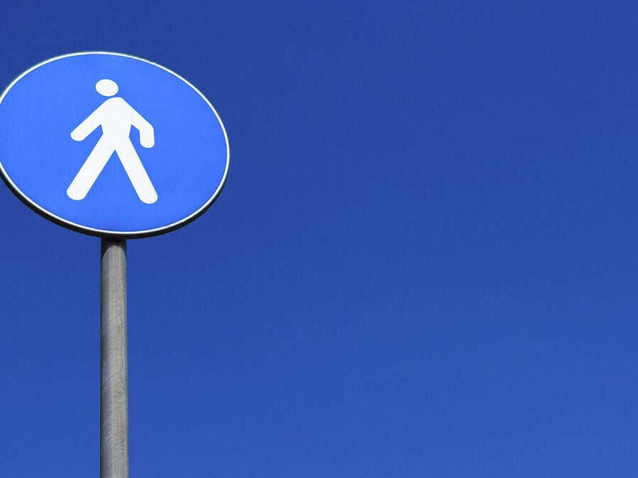 Blue pedestrian walkway sign on a bright blue sky background.